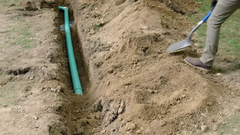 French drain trench mid-installation showing gravel and perforated pipe placement